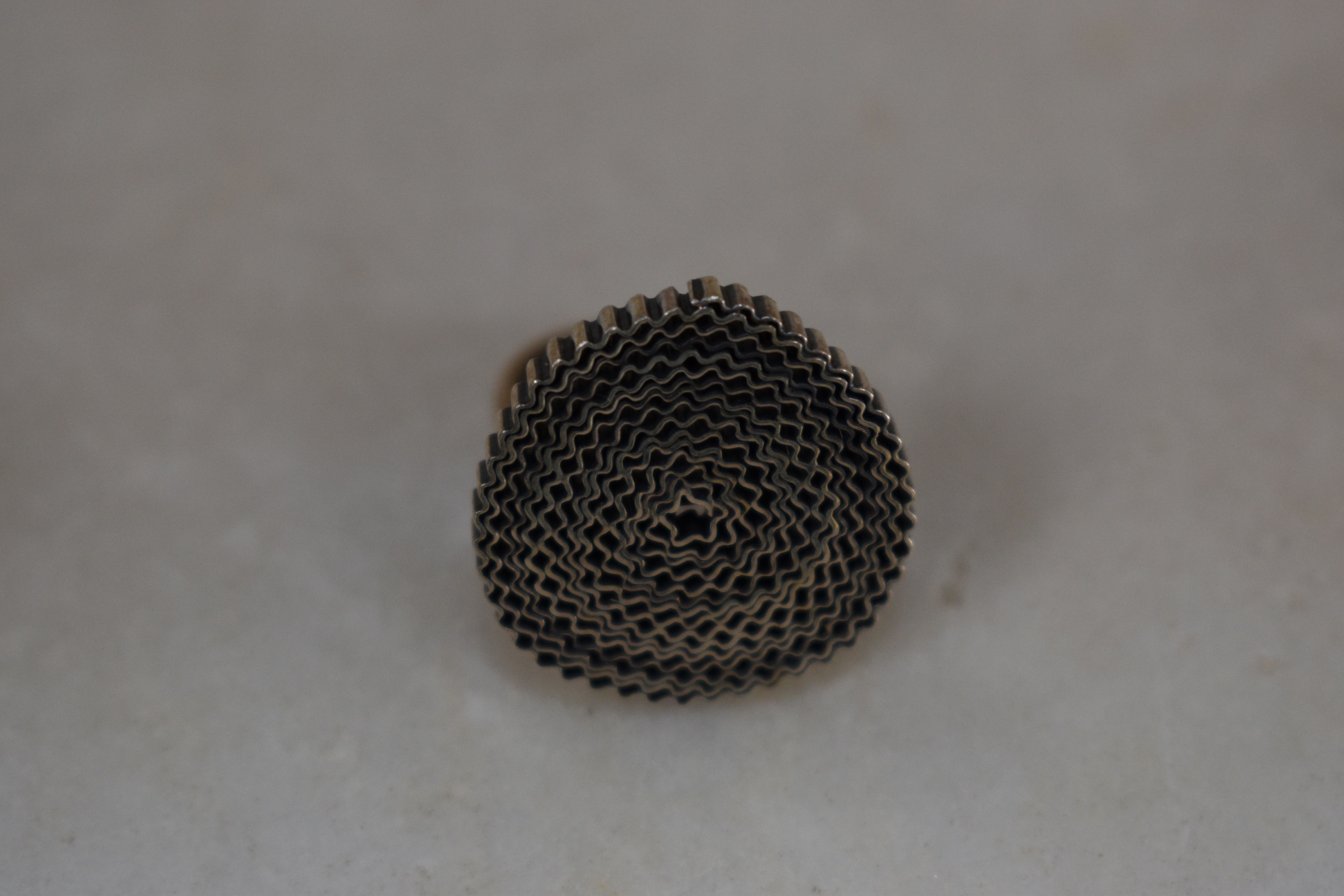 Το Σγουρό σε ουδέτερο φόντο ή γκαλερί, δείχνοντας τη γεωμετρική του μορφή και τη γυαλιστερή ασημένια επιφάνεια.